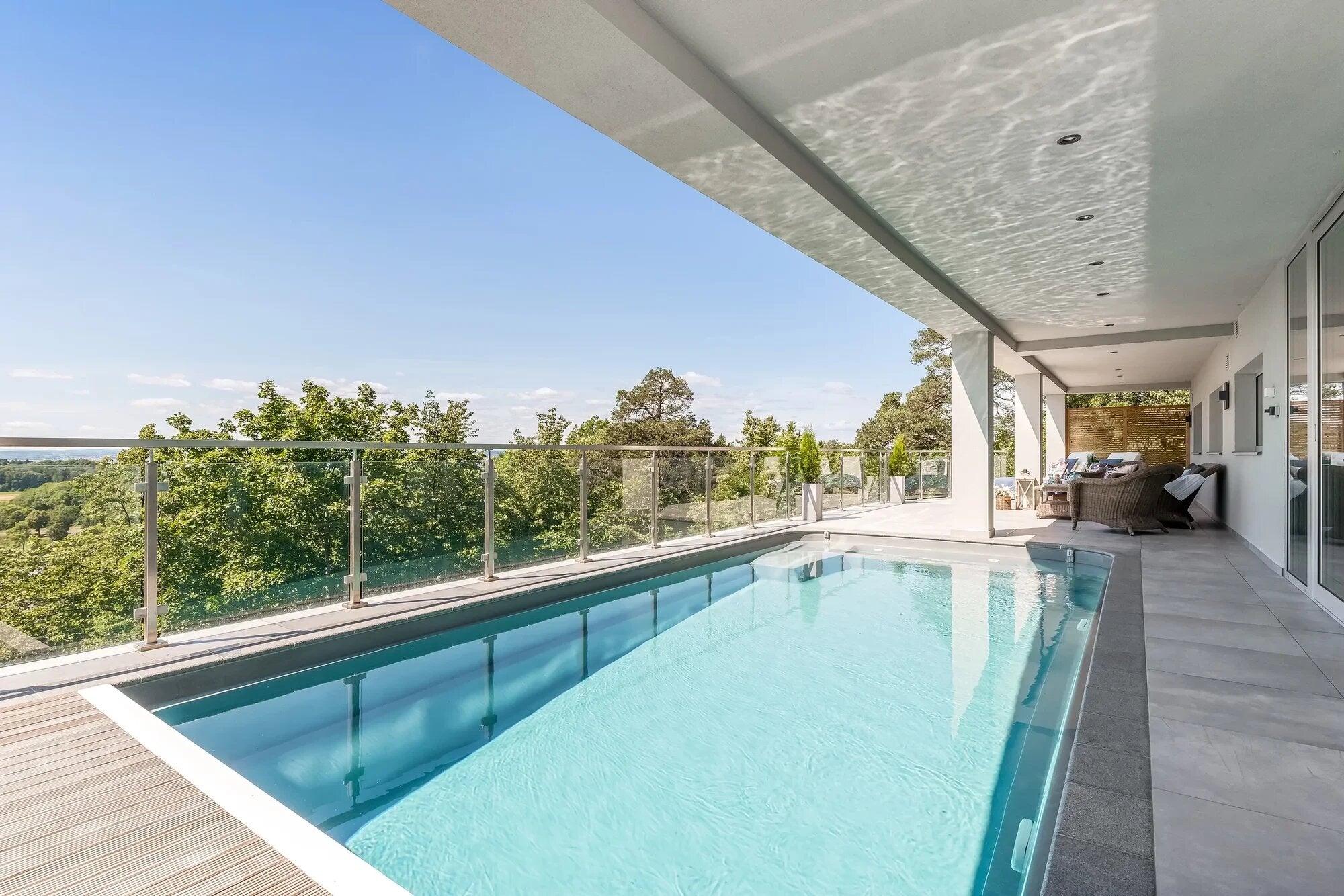 Piscină lungă pe terasa unei case moderne, cu vedere panoramică spre pădure