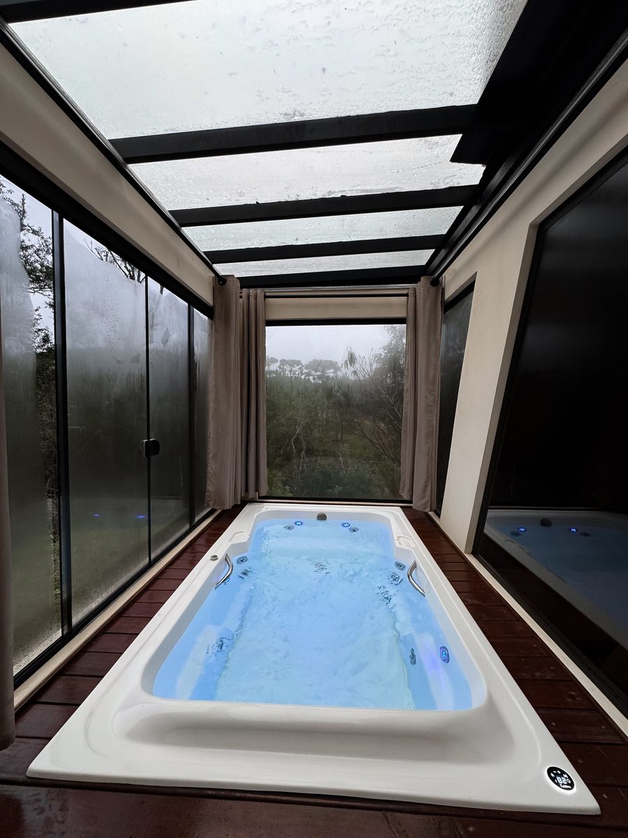 Cadă jacuzzi cu hidromasaj, iluminată în albastru, într-un spațiu cu pereți de sticlă