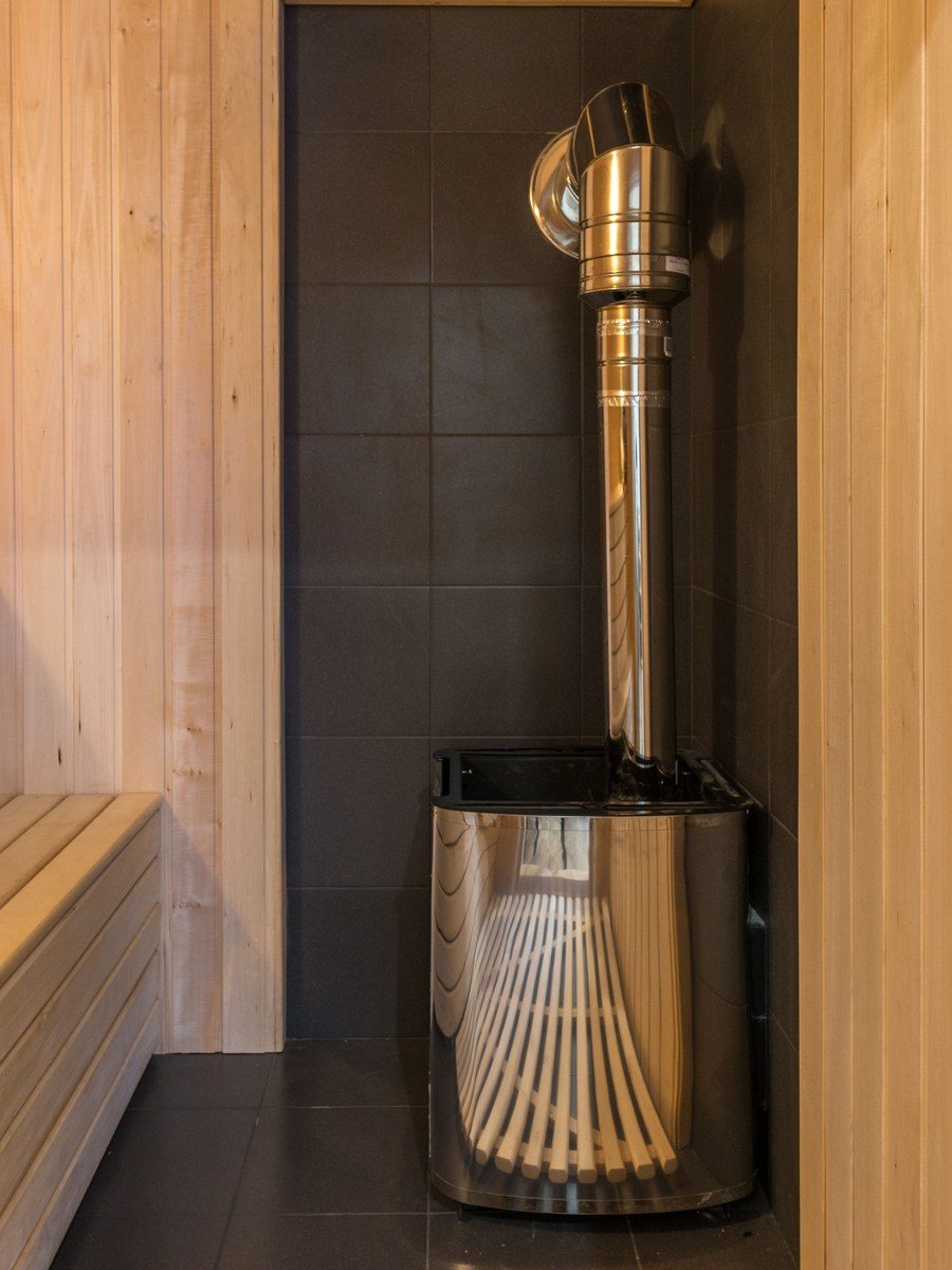 Saună modernă din lemn deschis la culoare, cu sobă din inox și cameră tehnică vizibilă